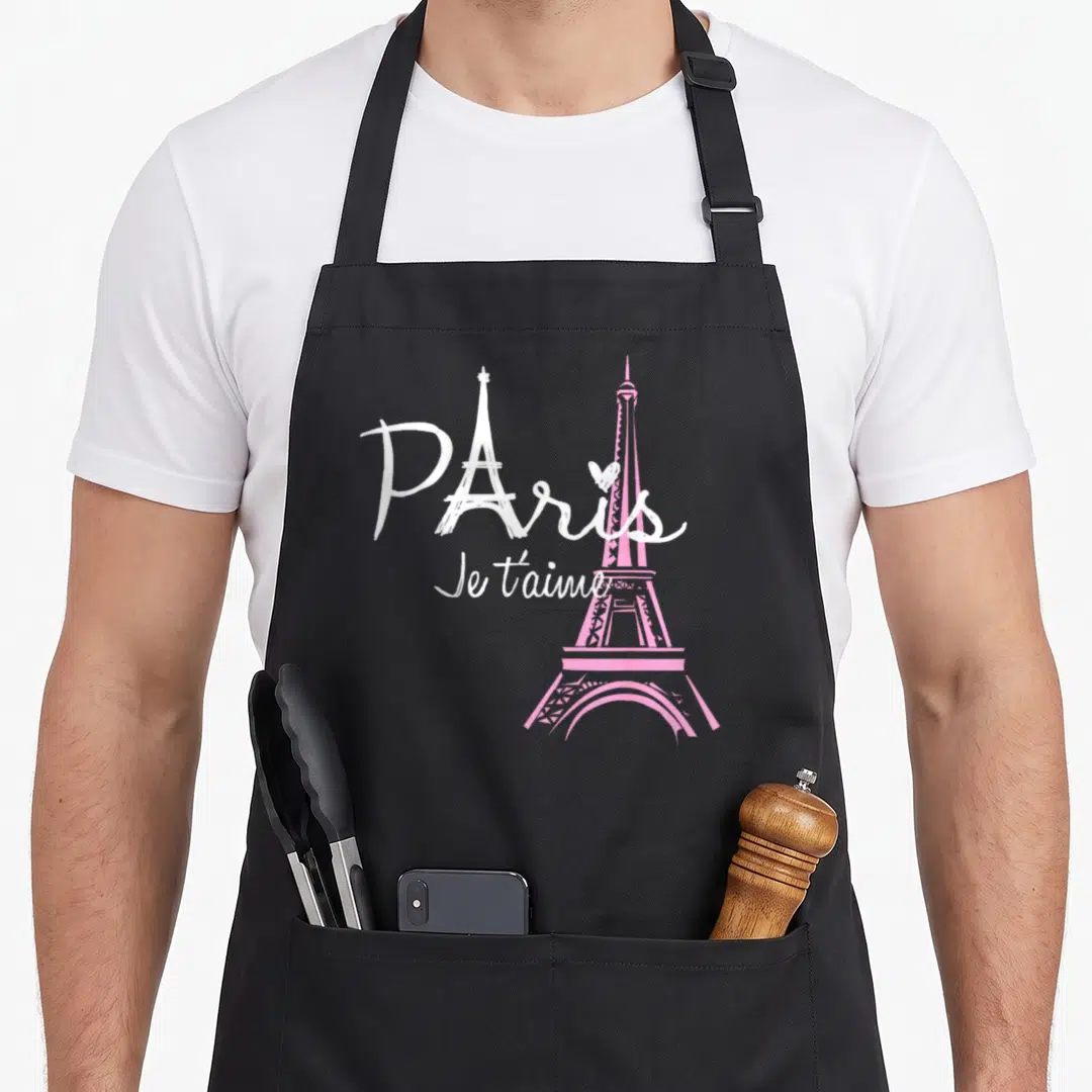 Eiffel paris apron - Paris Je t'aime text with white and pink Eiffel Tower silhouettes and small heart — shown on a black cotton canvas apron against a white background