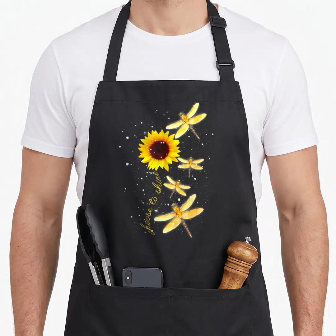 Dragonfly sunflower apron - Yellow sunflower and four dragonflies with white sparkles and curved script text — shown on a black cotton canvas apron against a white background