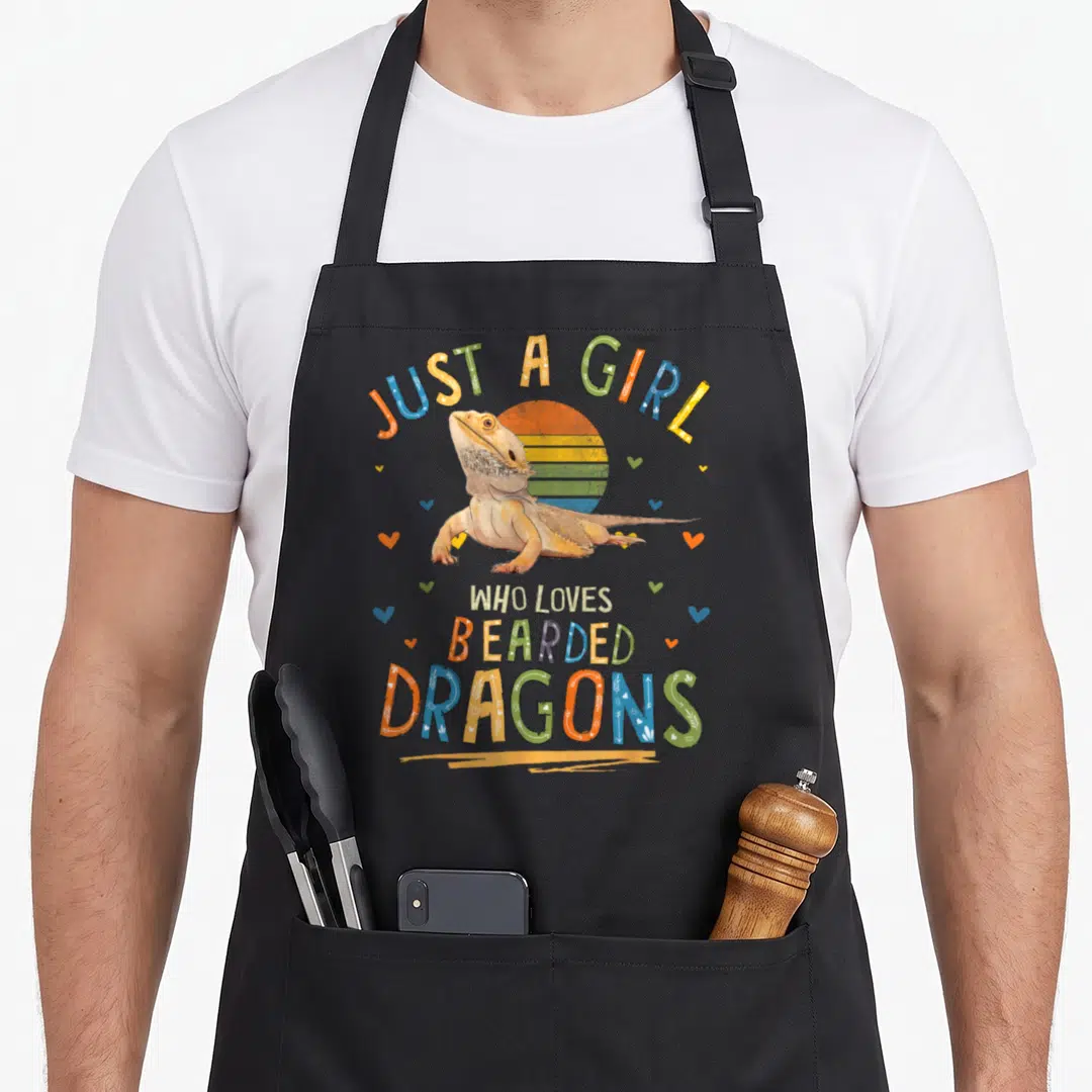 Bearded dragon apron - Cartoon bearded dragon with retro sun and Just A Girl Who Loves Bearded Dragons text — shown on a black cotton canvas apron against a white background