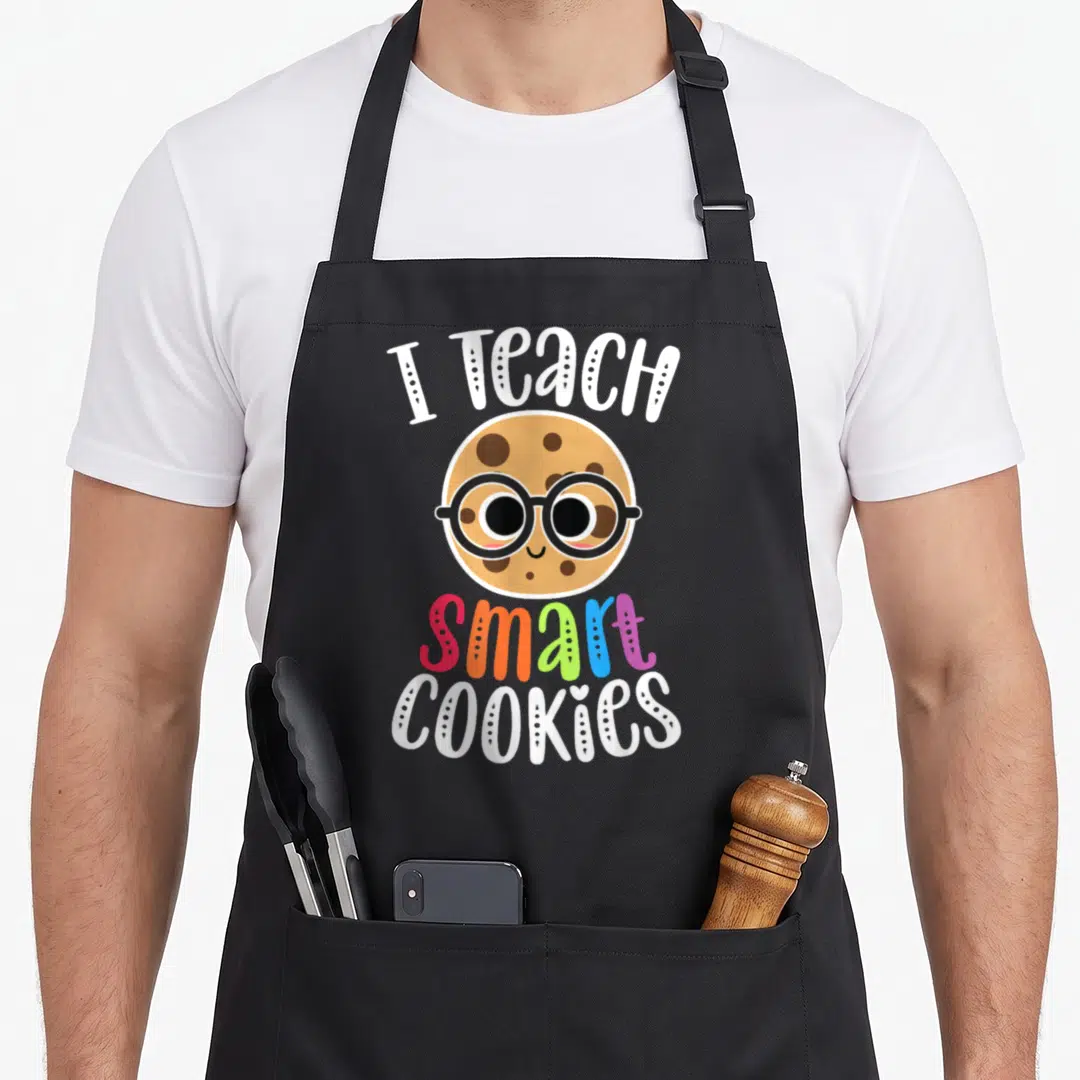 Teach cookies apron - Cartoon cookie with glasses and text I Teach Smart Cookies in white and multi-colored letters — shown on a black cotton canvas apron against a white background