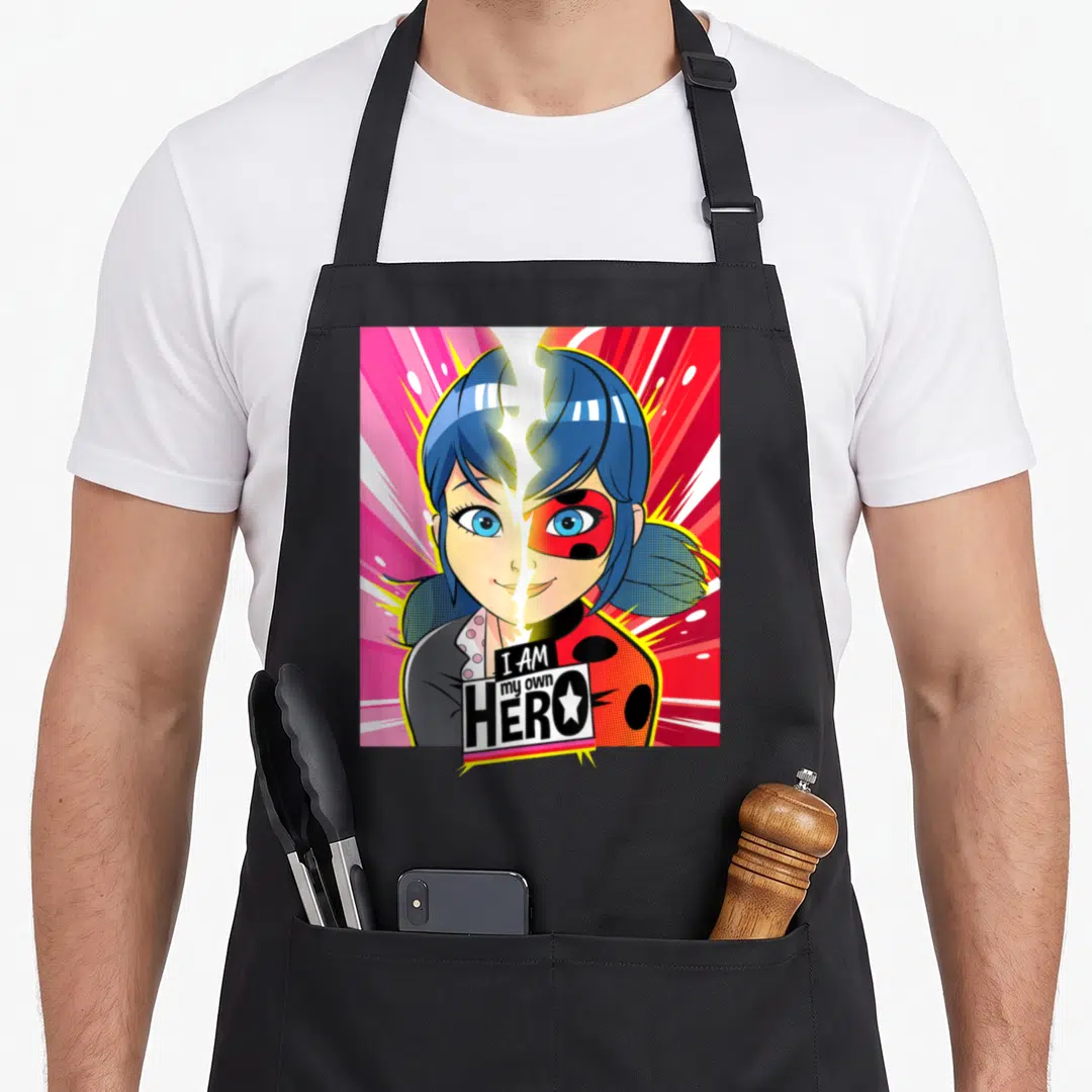 Miraculous ladybug apron - Split face girl portrait with I AM my own HERO text in blue red black and pink cartoon style — shown on a black cotton canvas apron against a white background