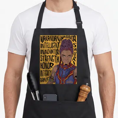 Shuri panther apron - Cartoon Shuri portrait with stacked text Intelligent Innovator Strength Honor Integrity Brave — shown on a black cotton canvas apron against a white background