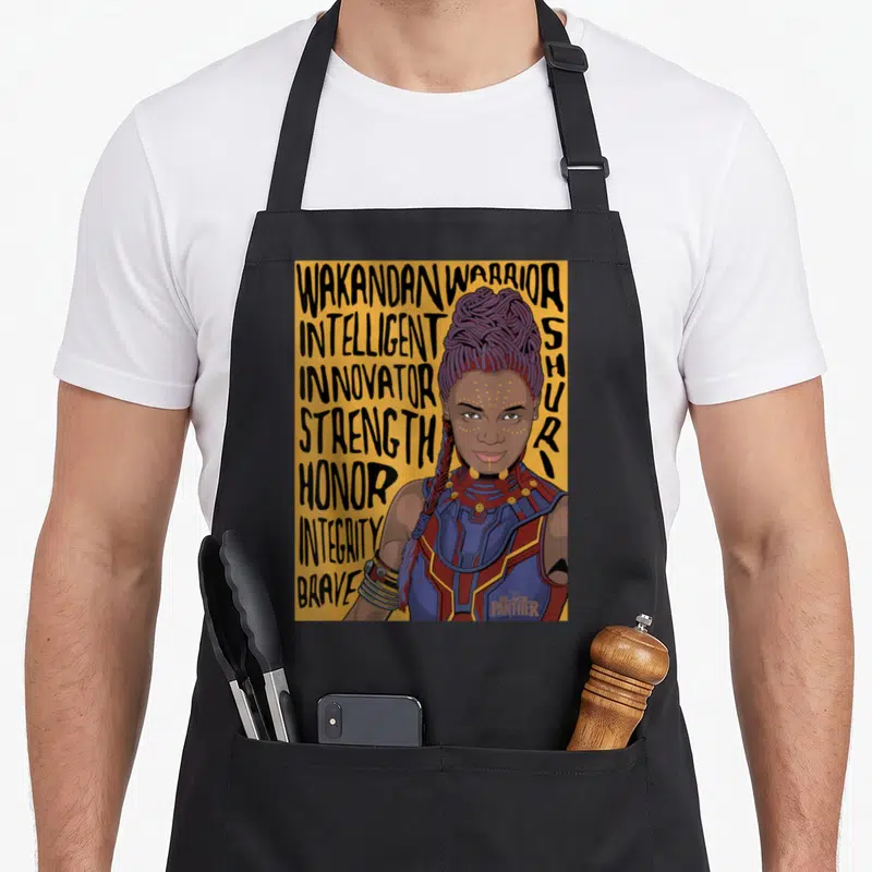 Shuri panther apron - Cartoon Shuri portrait with stacked text Intelligent Innovator Strength Honor Integrity Brave — shown on a black cotton canvas apron against a white background