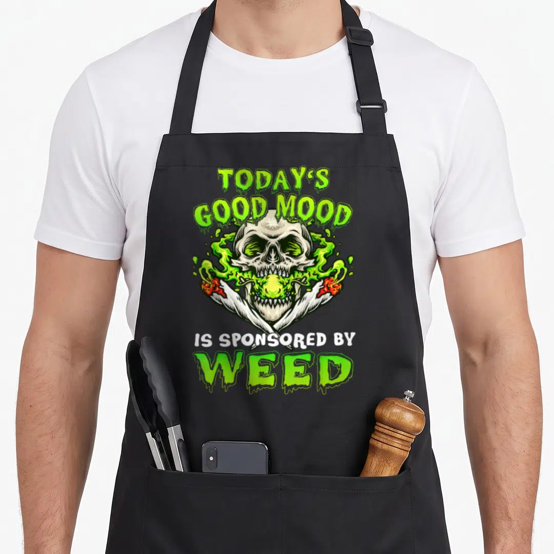 Leave smoking apron - Cartoon skull with lime smoke and two crossed joints reading TODAY'S GOOD MOOD IS SPONSORED — shown on a black cotton canvas apron against a white background