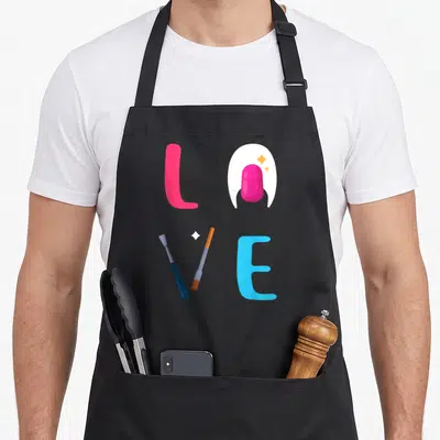 Tech artist manicurist apron - LOVE spelled with pink nail, blue pusher, orange file, and blue letter E in cartoon style — shown on a black cotton canvas apron against a white background