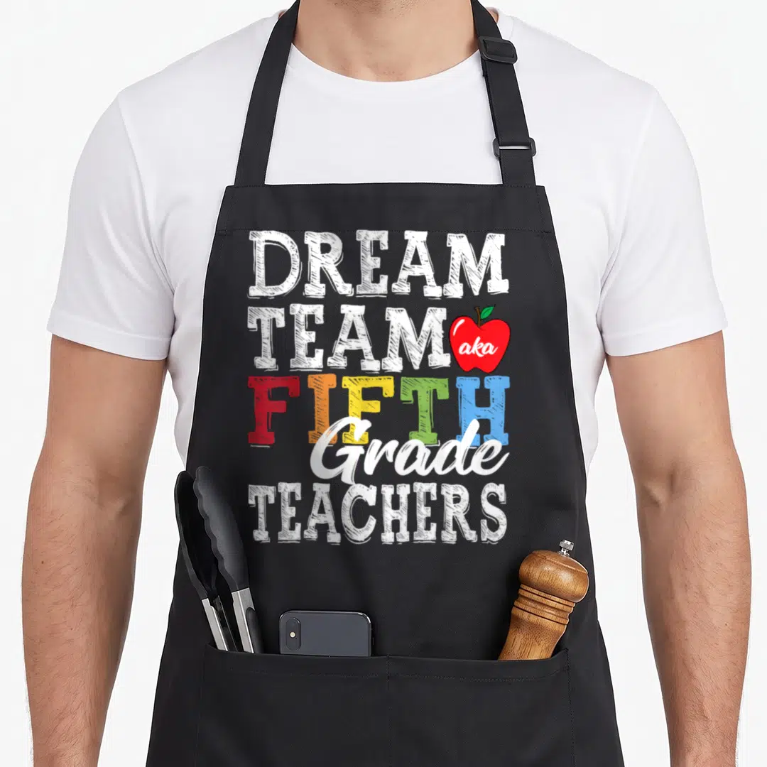 Aka teacher apron - Stacked text reading Dream Team Fifth Grade Teachers with red apple containing aka — shown on a black cotton canvas apron against a white background