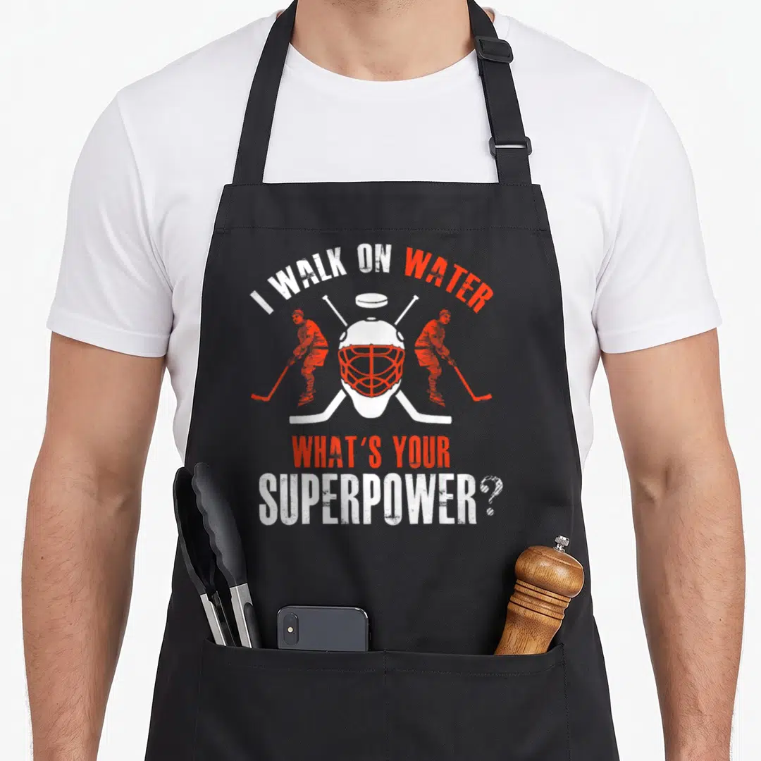 Hockey modern apron - Goalie mask with crossed sticks and I walk on water superpower text in white and red — shown on a black cotton canvas apron against a white background