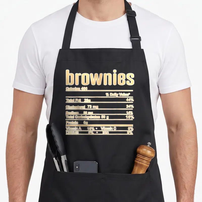 Browny christmas apron - beige nutrition facts label for brownies with calorie and fat data — shown on a black cotton canvas apron against a white background