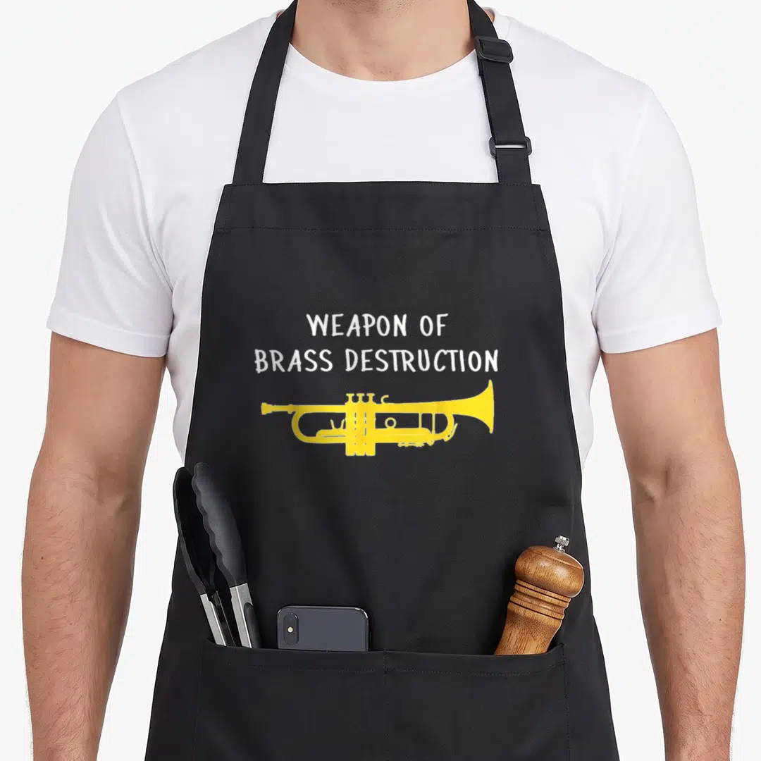 Weapon trumpet apron - White text reading Weapon of Brass Destruction above yellow trumpet silhouette — shown on a black cotton canvas apron against a white background