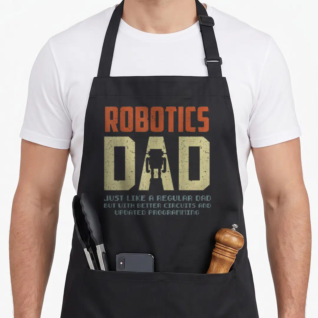 Robotic father day apron - Stacked orange-red and beige text reading Robotics Dad with robot silhouette in letter — shown on a black cotton canvas apron against a white background