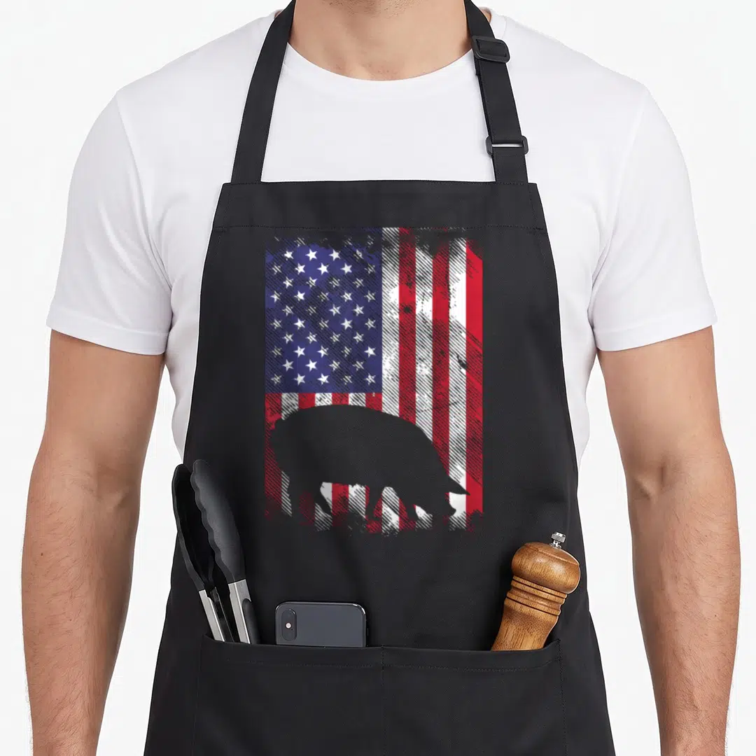 Flag farmers apron - Grey pig silhouette overlaid on a distressed red white and blue American flag pattern — shown on a black cotton canvas apron against a white background