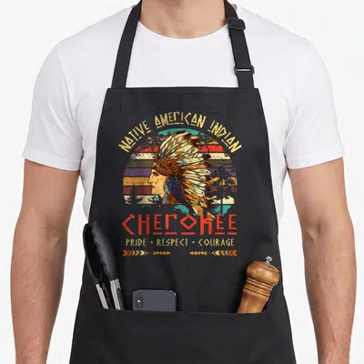 Indigenous tribe native american apron - Cherokee man profile, striped sun, pride respect courage text, distressed — shown on a black cotton canvas apron against a white background