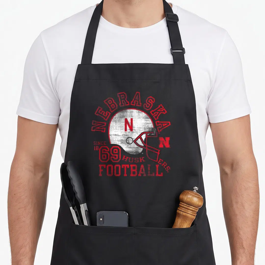 Cornhusker football apron - Distressed red Nebraska helmet graphic with arched text and since 1869 inscription — shown on a black cotton canvas apron against a white background