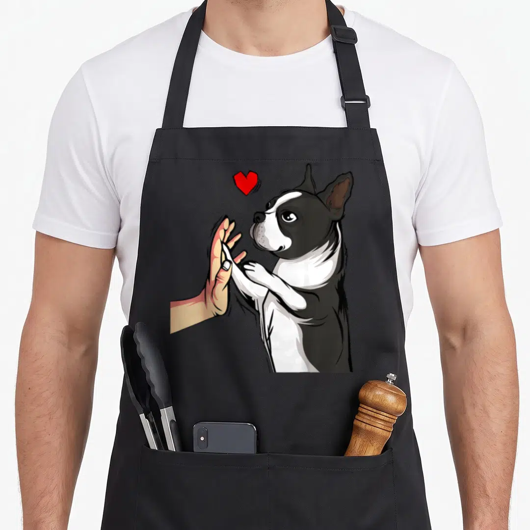 Boston terrier dog apron - Cartoon black and white dog high-fiving a hand with a red heart above — shown on a black cotton canvas apron against a white background