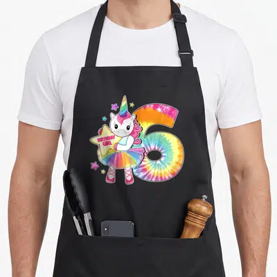6th tie-dye apron - Cartoon unicorn holding BIRTHDAY GIRL star next to tie-dye number 6 — shown on a black cotton canvas apron against a white background
