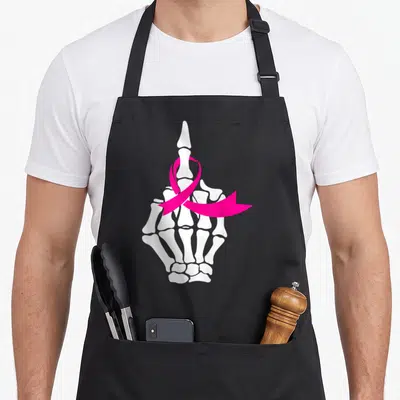 Middle ribbon apron - White skeleton hand with pink ribbon wrapped around middle finger — shown on a black cotton canvas apron against a white background