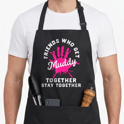 Mud friends apron - Pink handprint with white text Friends Who Get Muddy Together Stay Together — shown on a black cotton canvas apron against a white background