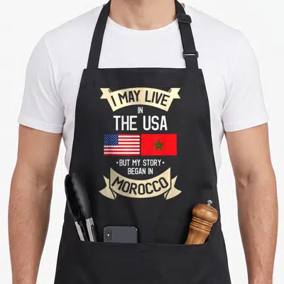 Morocco moroccan american flag apron - Stacked text with US and Morocco flags side-by-side inside beige ribbons — shown on a black cotton canvas apron against a white background