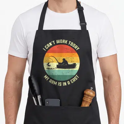 Today arm father day apron - Fisherman silhouette in boat against striped sun with text I CAN'T WORK TODAY MY ARM IS — shown on a black cotton canvas apron against a white background