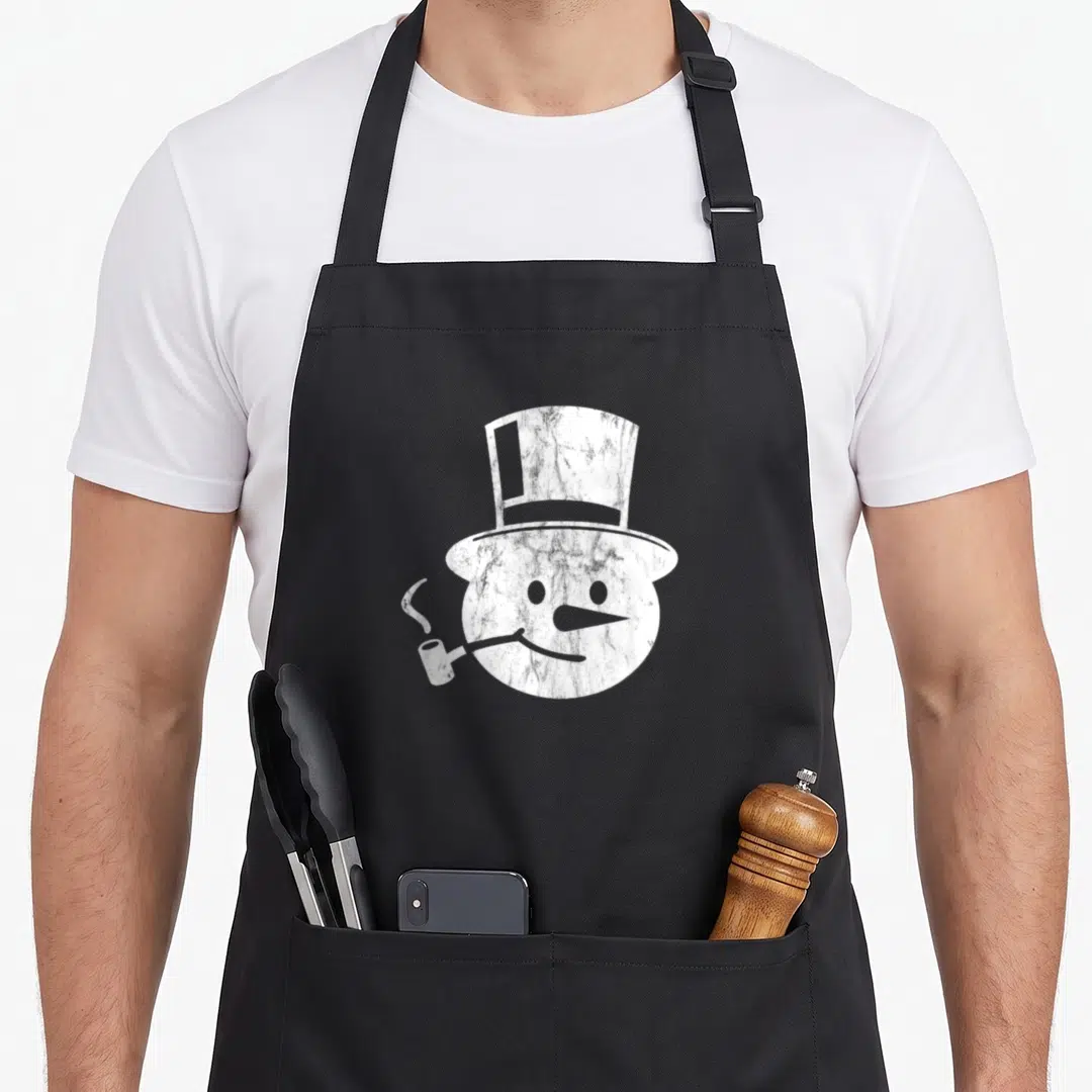 Santas christmas snowman apron - White distressed snowman head wearing a top hat and holding a smoking pipe — shown on a black cotton canvas apron against a white background