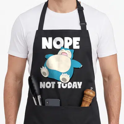 Sleeping snorlax apron - Blue cartoon snorlax lying down between NOPE and NOT TODAY text — shown on a black cotton canvas apron against a white background
