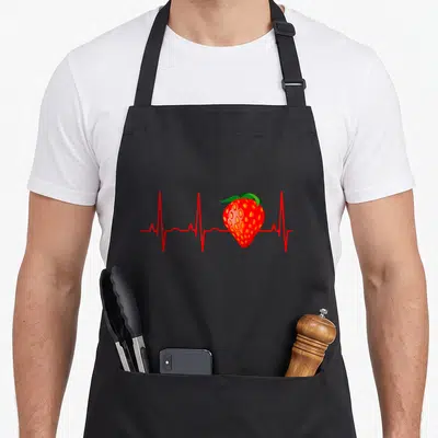 Heartbeat strawberry apron - Red strawberry overlapping a red heartbeat line with green leaves — shown on a black cotton canvas apron against a white background