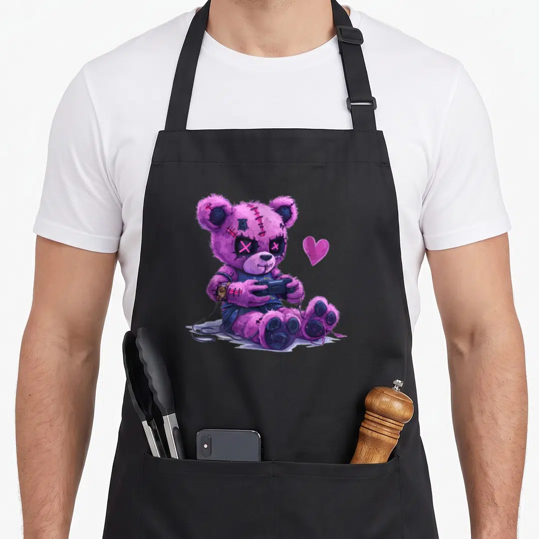 Creepy teddy bear apron - Purple stitched teddy bear holding game controller with pink heart and wires — shown on a black cotton canvas apron against a white background