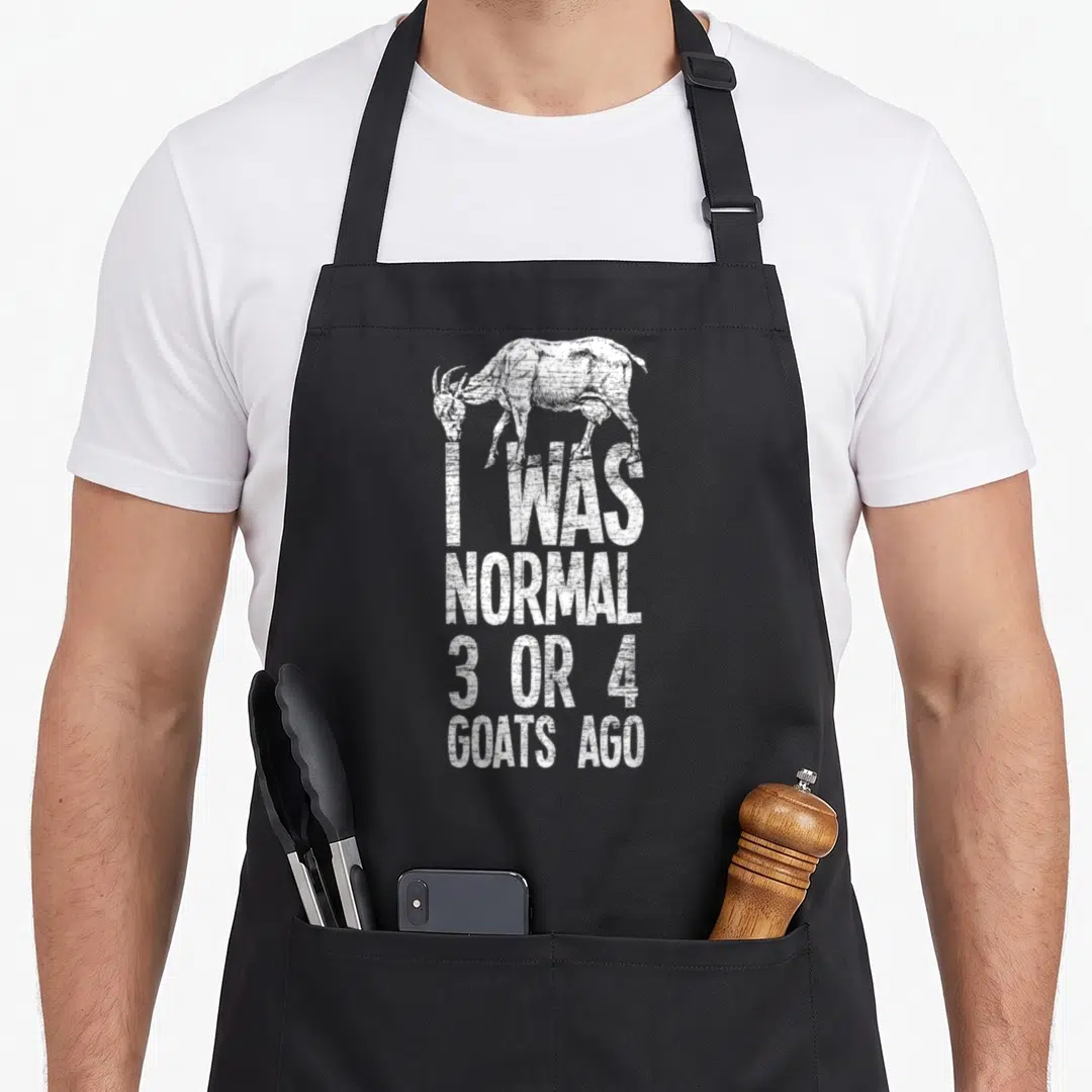 Three goat apron - White distressed goat illustration above stacked text I WAS NORMAL 3 OR 4 GOATS AGO — shown on a black cotton canvas apron against a white background