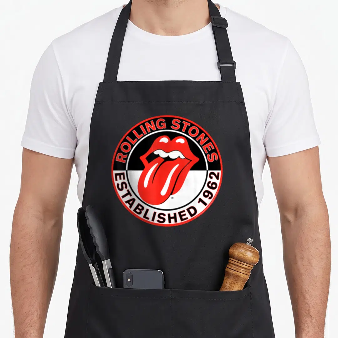 Est rolling stones apron - Red mouth and tongue over black and white split background with established 1962 text — shown on a black cotton canvas apron against a white background