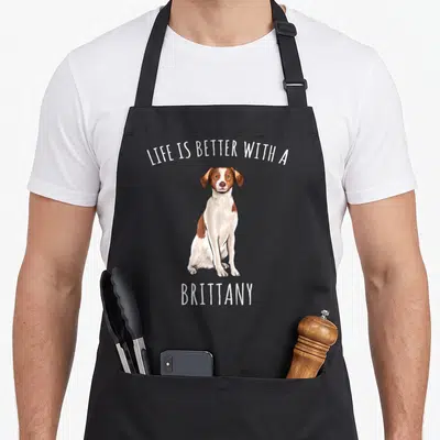 Better brittany dog apron - Cartoon Brittany dog sitting with LIFE IS BETTER WITH A BRITTANY text in white — shown on a black cotton canvas apron against a white background