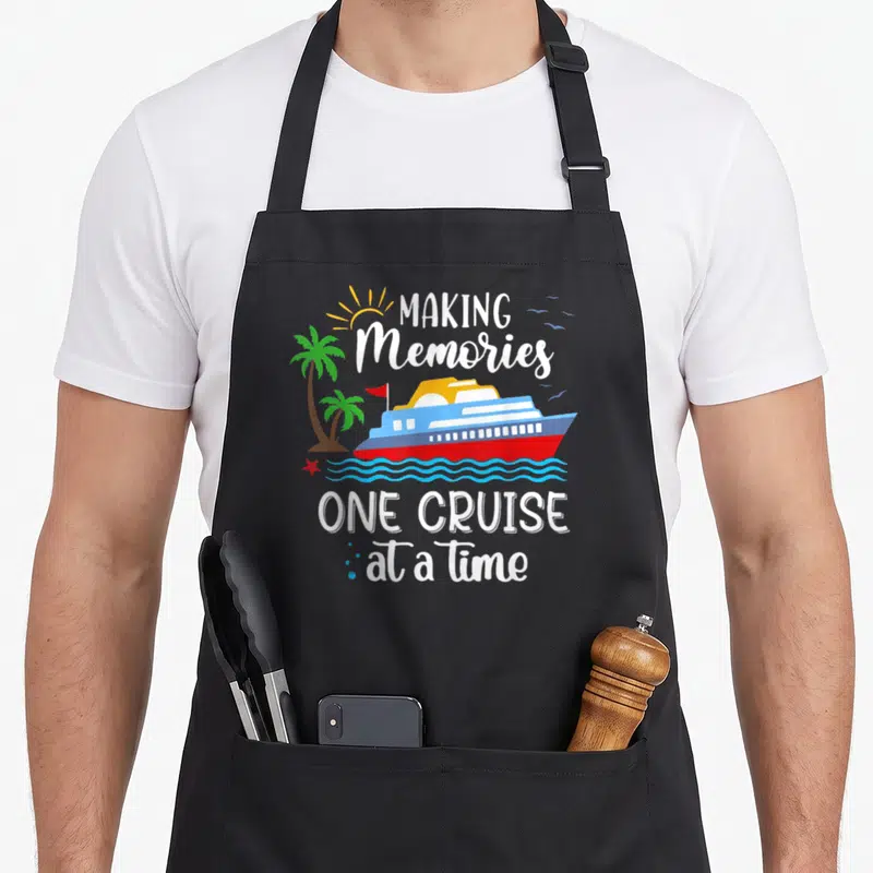 Cruise memory apron - Cartoon cruise ship on blue waves with palm trees and text Making Memories One Cruise At A Time — shown on a black cotton canvas apron against a white background