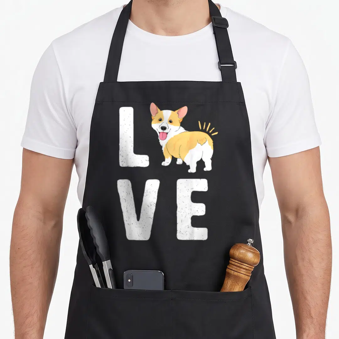 Puppy welsh apron - Cartoon corgi replacing O in white textured LOVE text — shown on a black cotton canvas apron against a white background
