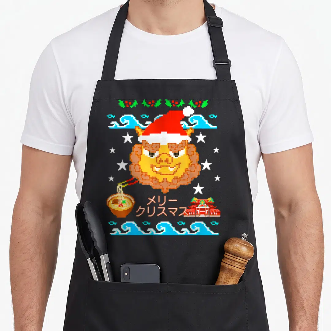 Shisa ugly sweater apron - Pixel art lion head in santa hat with waves, ramen, temple, holly, and Japanese text — shown on a black cotton canvas apron against a white background