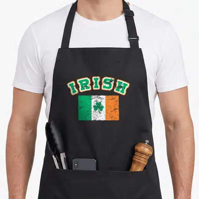 Eire ireland apron - Arched IRISH text above distressed green white orange flag with centered green shamrock — shown on a black cotton canvas apron against a white background