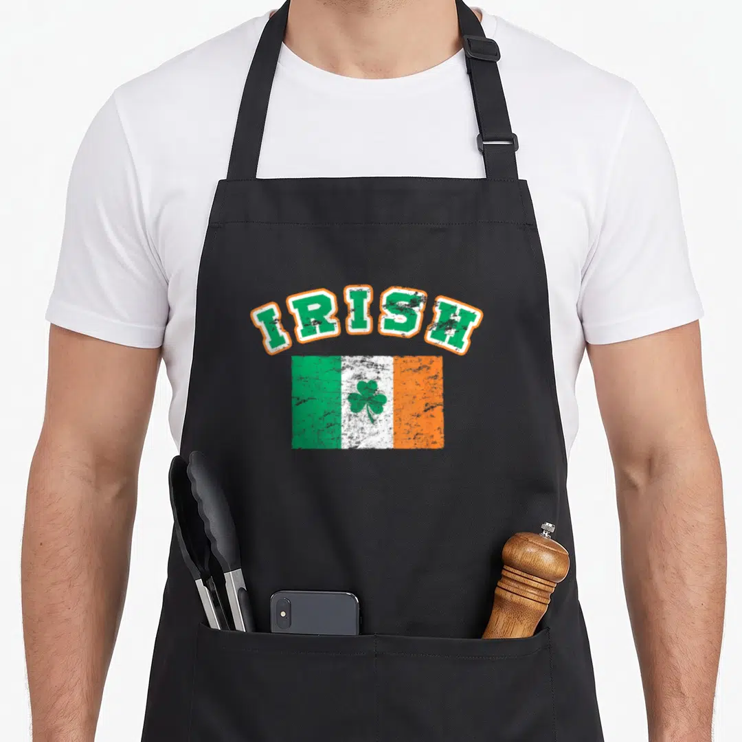 Eire ireland apron - Arched IRISH text above distressed green white orange flag with centered green shamrock — shown on a black cotton canvas apron against a white background