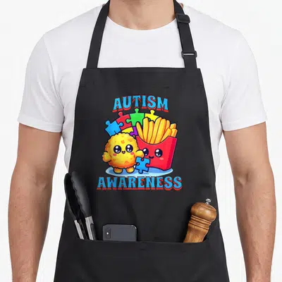 French chicken apron - Cartoon fries and nugget holding puzzle pieces under autism awareness text — shown on a black cotton canvas apron against a white background