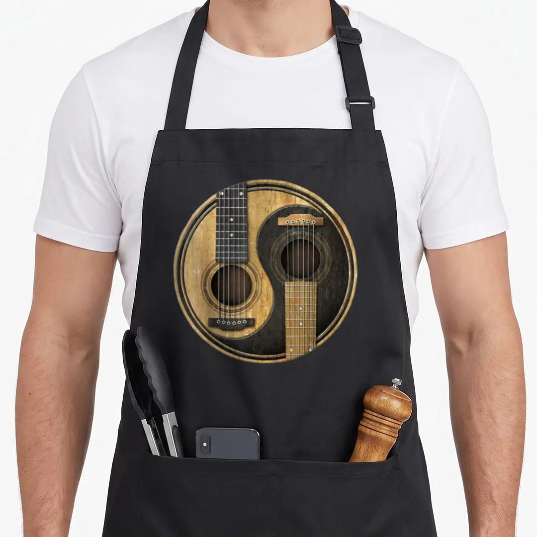 Ying guitarist apron - Two acoustic guitars arranged in a circular yin yang pattern with tan and black wood textures — shown on a black cotton canvas apron against a white background