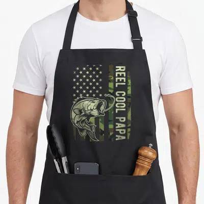 Fisherman american flag apron - Bass fish and hook over camo flag with vertical Reel Cool Papa text — shown on a black cotton canvas apron against a white background