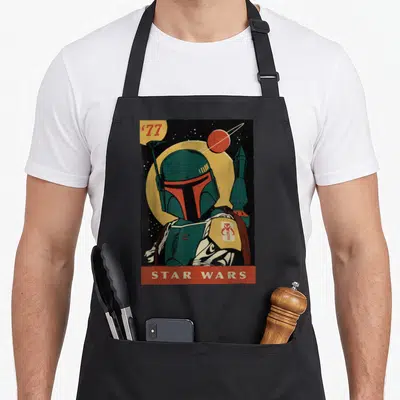 Trading boba apron - Retro 1977 Boba Fett illustration with yellow moon and red planet in teal and red colors — shown on a black cotton canvas apron against a white background