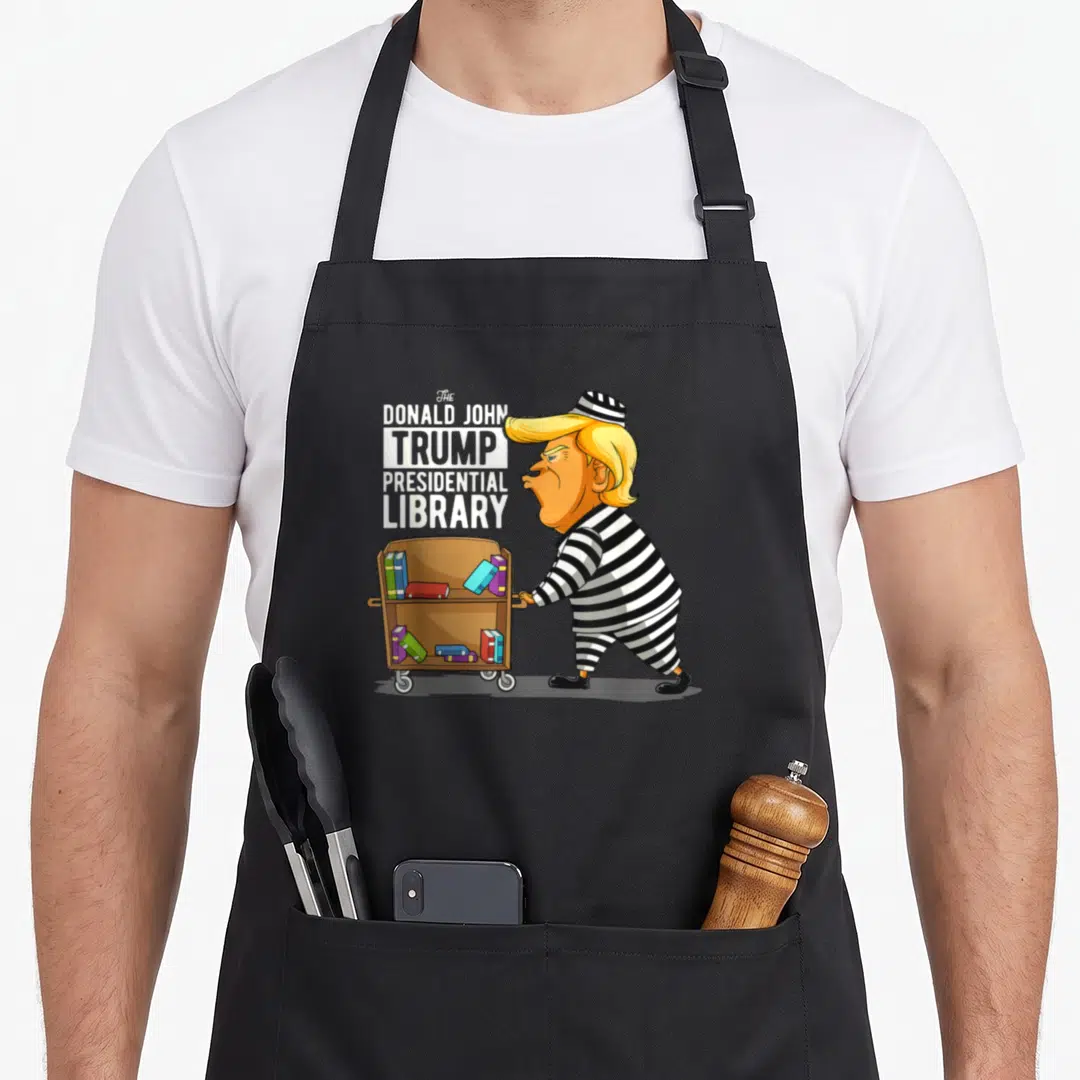 Prison option funny apron - Cartoon man in striped uniform pushing brown book cart next to stacked text reading — shown on a black cotton canvas apron against a white background