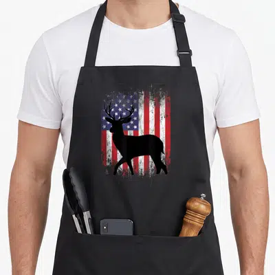Deer hunting grill hunter apron - Black deer silhouette standing before a distressed red white and blue American flag — shown on a black cotton canvas apron against a white background
