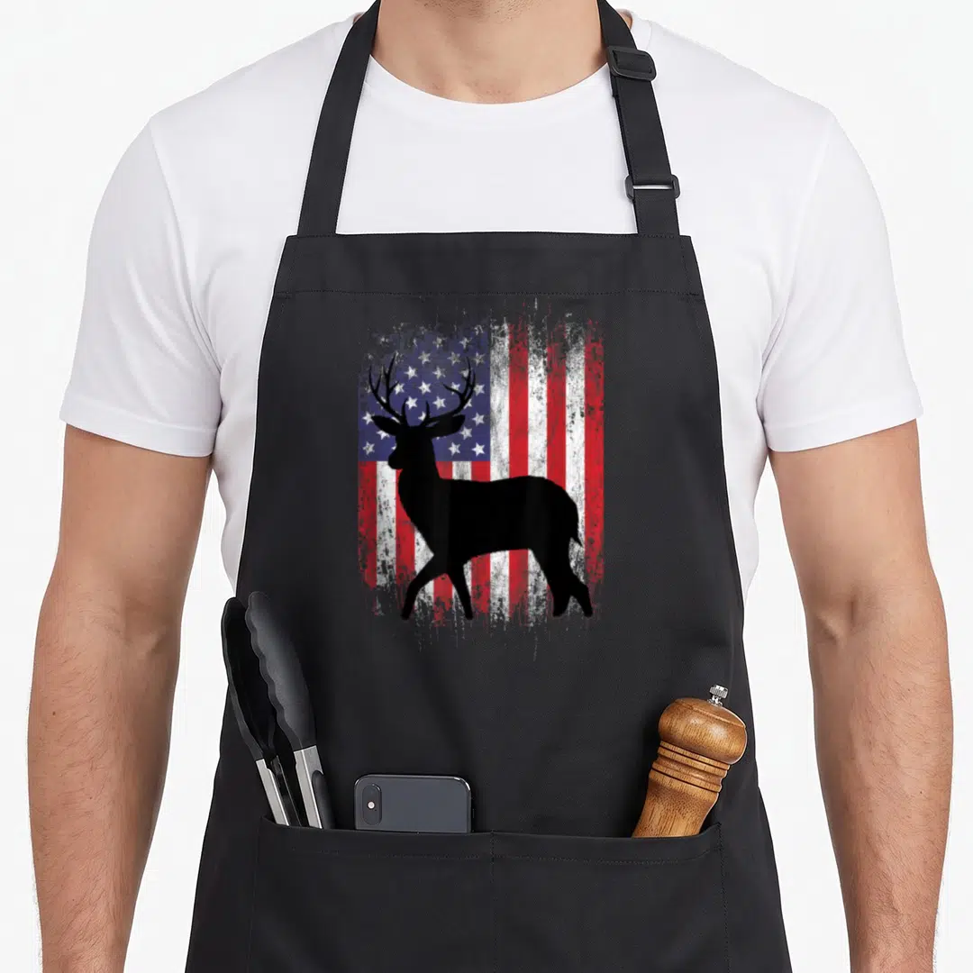 Deer hunting grill hunter apron - Black deer silhouette standing before a distressed red white and blue American flag — shown on a black cotton canvas apron against a white background