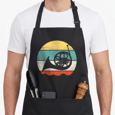 Funny horn french apron - Grey french horn silhouette over four horizontal stripes in yellow, teal, white, and orange — shown on a black cotton canvas apron against a white background