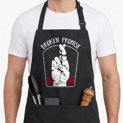 Broken kawaii cooking apron - BROKEN PROMISE text over hand with separated fingers and red roses — shown on a black cotton canvas apron against a white background
