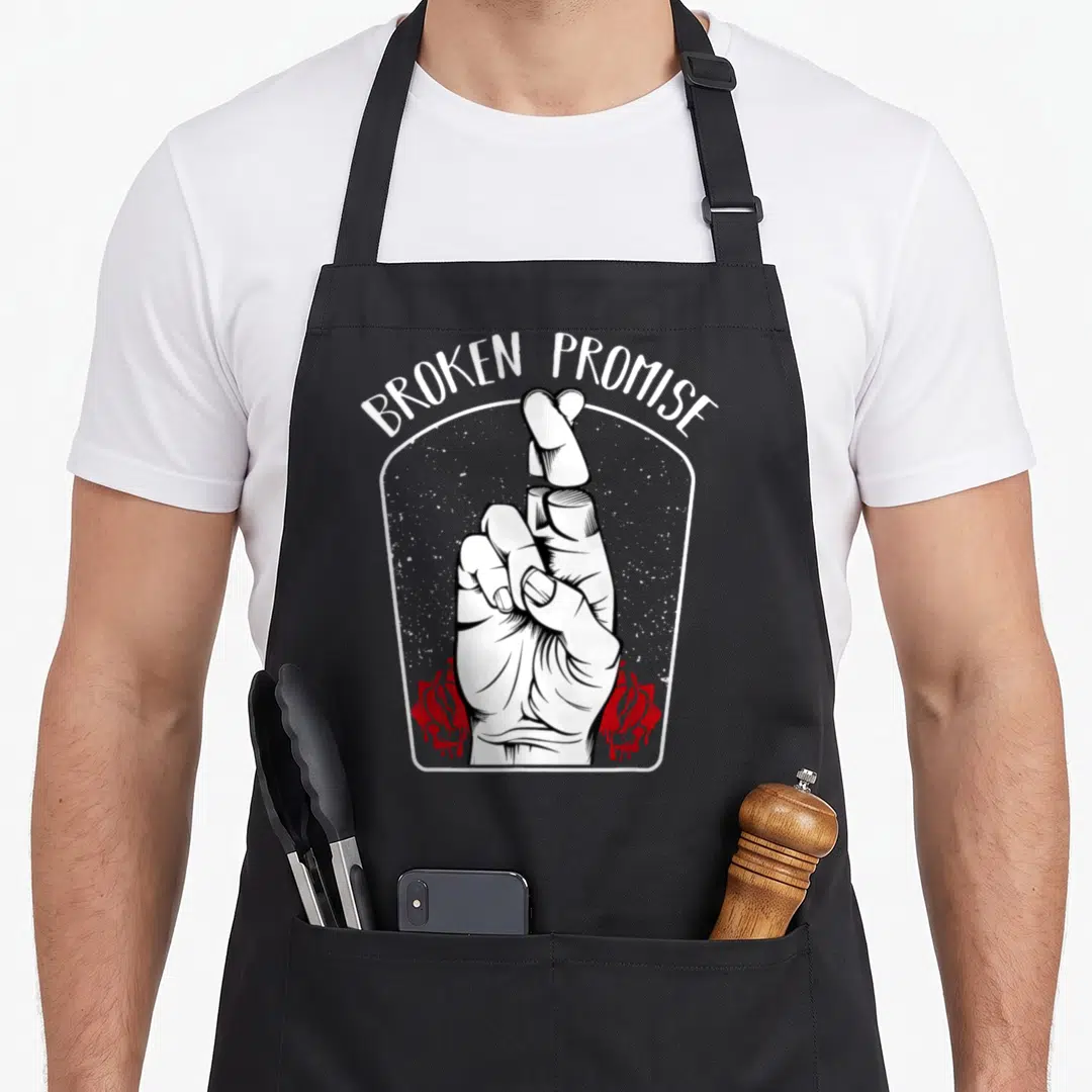 Broken kawaii cooking apron - BROKEN PROMISE text over hand with separated fingers and red roses — shown on a black cotton canvas apron against a white background