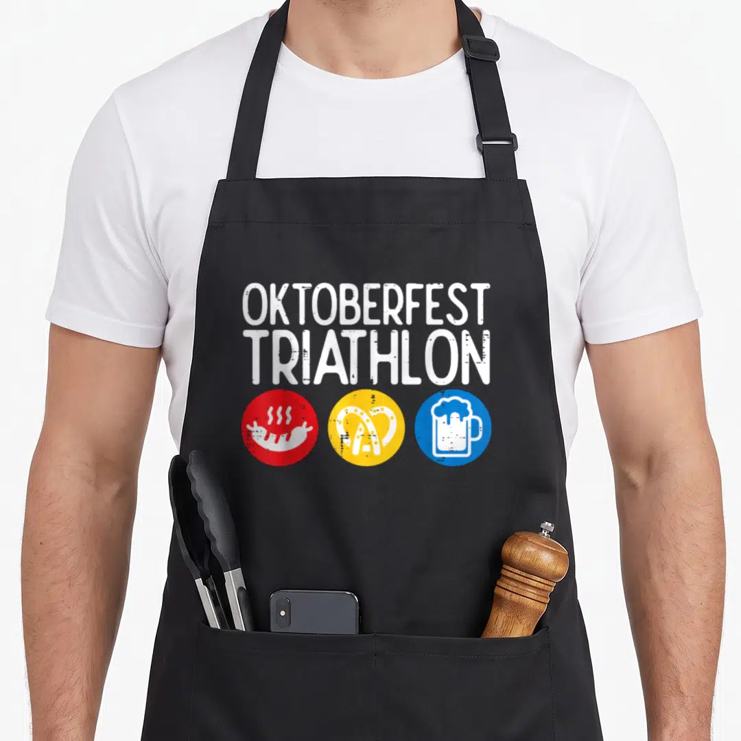 Triathlon oktoberfest apron - Distressed white OKTOBERFEST TRIATHLON text above red sausage, yellow pretzel, and blue — shown on a black cotton canvas apron against a white background