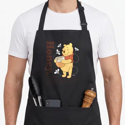 Definition honey apron - Winnie the Pooh holding pot beside vertical Honey text and definition with bees and dotted — shown on a black cotton canvas apron against a white background