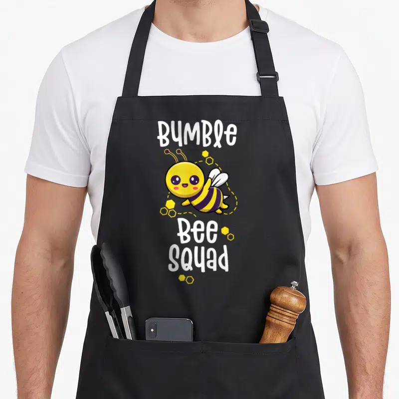 Bumble cute teacher aprons - Cartoon bee with BUMBLE Bee SQUAD text and yellow honeycomb cells — shown on a black cotton canvas apron against a white background