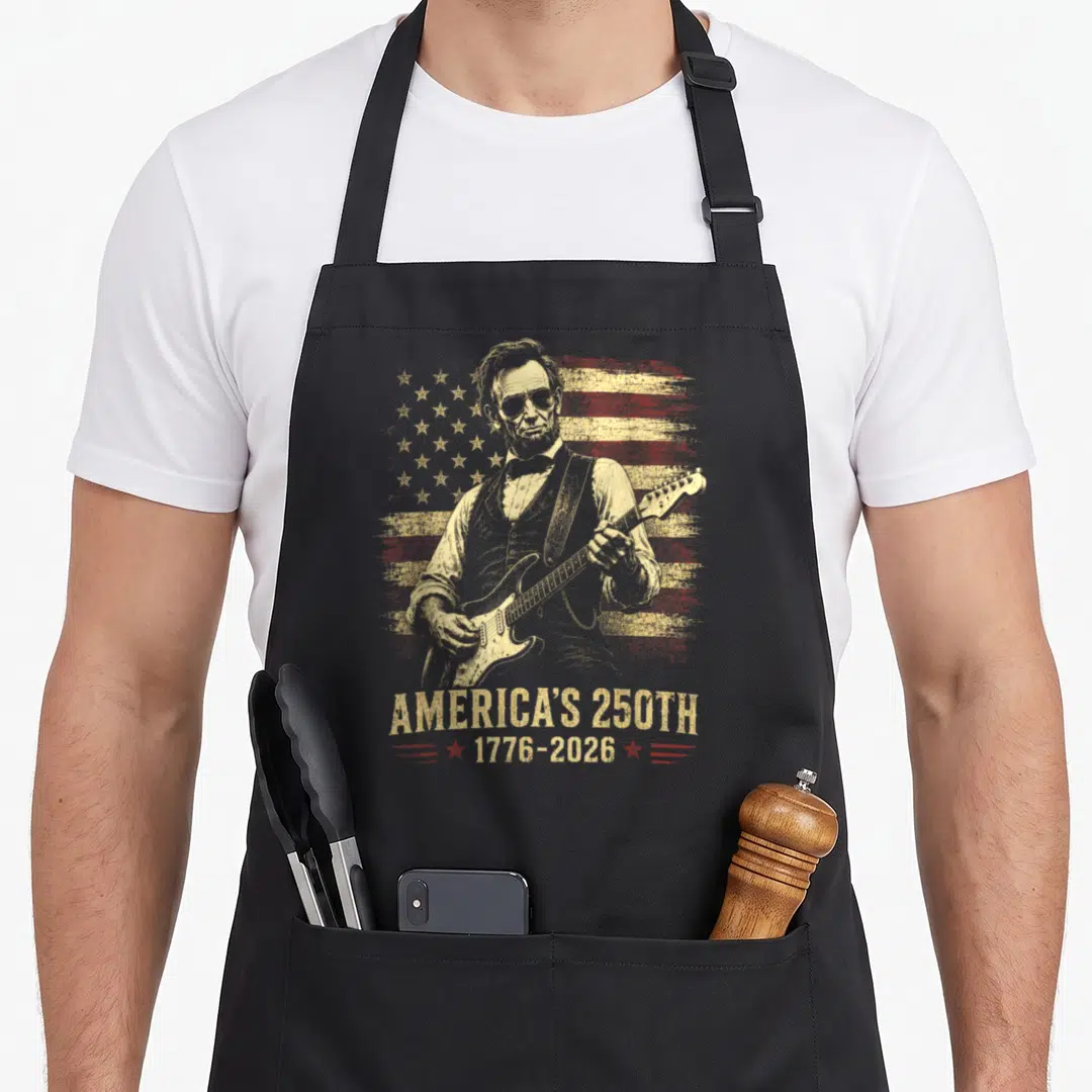 Abraham 250th 4th of july apron - Abraham Lincoln playing guitar over distressed red and gold flag with America's 250th — shown on a black cotton canvas apron against a white background