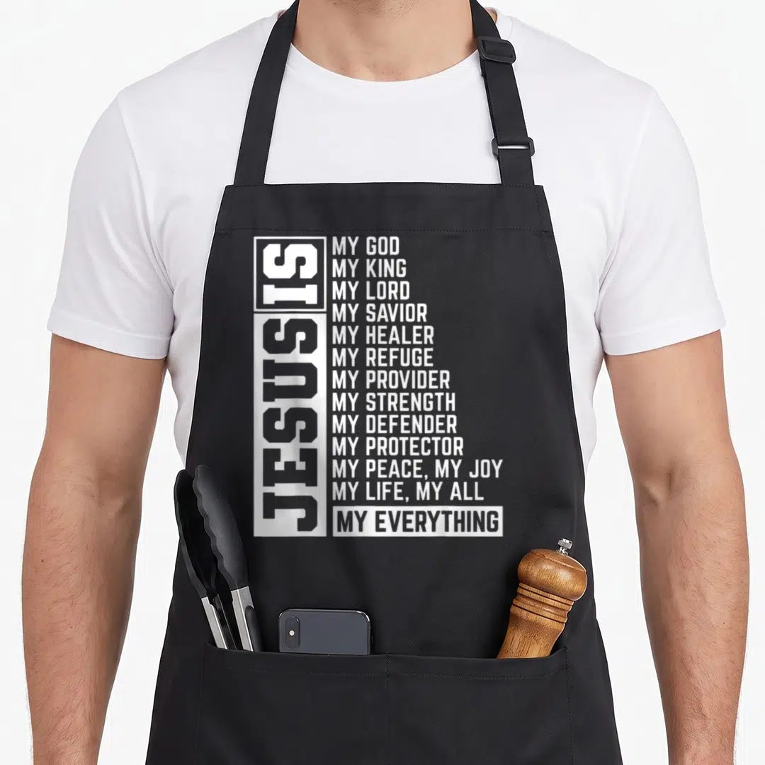 Lord christian aprons - White vertical Jesus Is text beside horizontal list of divine attributes on dark background — shown on a black cotton canvas apron against a white background